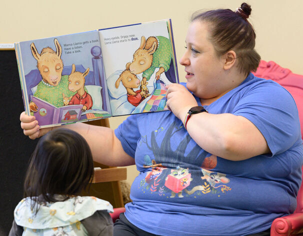 Librarian holding up a book while an interested child looks on