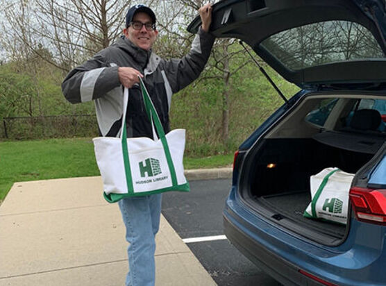 Library staff at car holding delivery bag with library logo