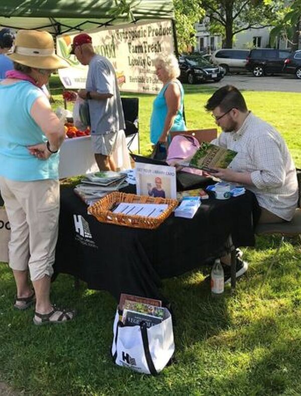Library staff member seated at outdoor table at Farmers Market